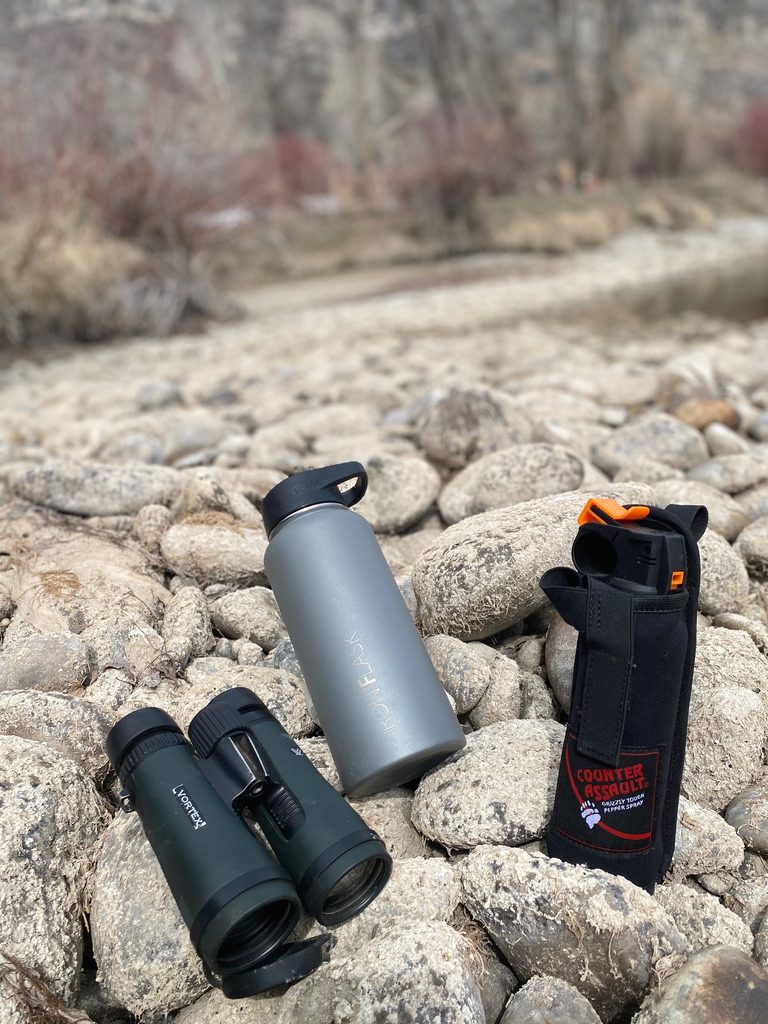 Iron Flask next to binoculars and bear spray. 